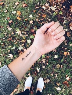 a woman's arm with a small tattoo on it, in front of leaves