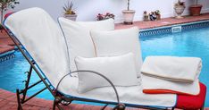 a chair with some pillows on it next to a swimming pool and potted plants