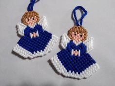 two cross stitch angel ornaments hanging from blue ribbones on a white tablecloth background