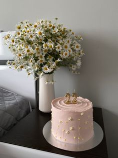 a pink cake sitting on top of a table next to a vase filled with flowers