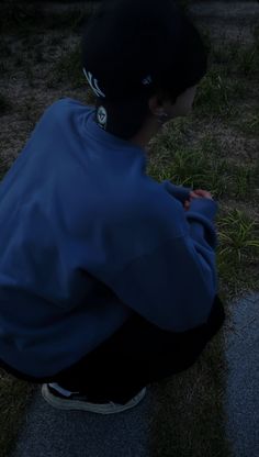 a young man sitting on the ground looking at his cell phone while wearing a blue jacket