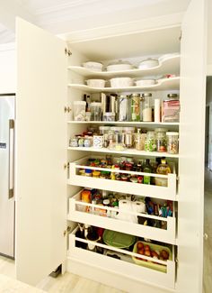 an organized pantry in the corner of a kitchen with white cupboards and shelves filled with food