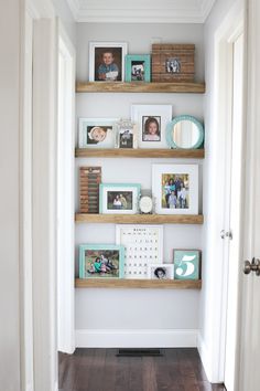 some shelves with pictures on them in a room that is painted white and has wood flooring