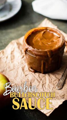 a bowl of butterscotch sauce sitting on top of a piece of wax paper next to an apple