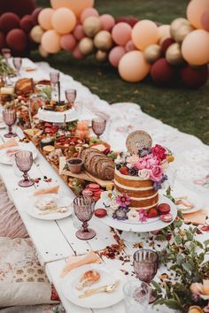 a table topped with lots of food and desserts next to balloons in the background