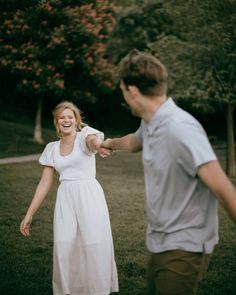 a man and woman are holding hands in the grass, with trees in the background