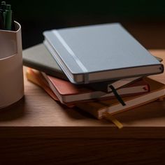 a stack of books sitting on top of a wooden table next to a cup and pen