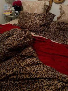 a leopard print comforter on a bed with red sheets and pillows, in front of a round mirror