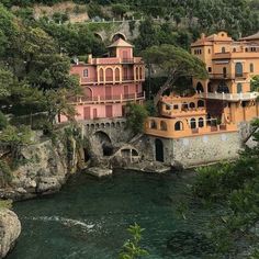 some buildings are on the side of a cliff by the water in front of trees