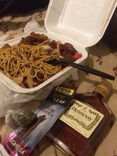 a plastic container filled with noodles and meat next to bottles of alcohol on a table