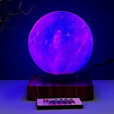 the moon lamp is on top of a wooden stand with a remote control in front of it