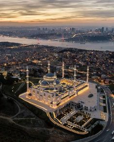 an aerial view of a large white building with lights on it's sides and the city in the background