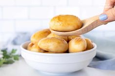 a person holding a wooden spoon over a bowl of doughnuts