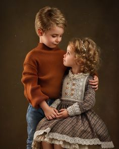 two young children are hugging each other in front of a brown background and the boy is wearing an orange sweater