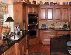 a large kitchen with wooden cabinets and black counter tops on the island in front of the sink