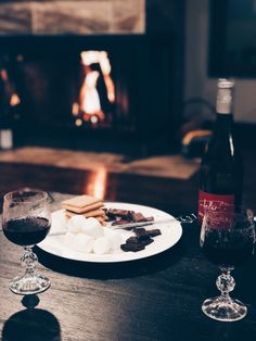 a plate with marshmallows, chocolate and wine next to a fire place