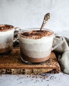 two mugs filled with hot chocolate and whipped cream on top of a wooden cutting board