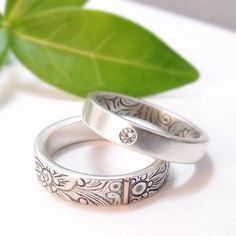 two wedding rings sitting next to each other on top of a white surface with a green leaf in the background