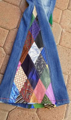 a pair of blue jeans with colorful patchwork on the bottom and side, sitting on a brick floor