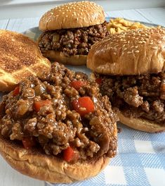 three hamburgers with meat and vegetables are on a blue checkered table cloth next to bread