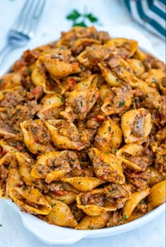 pasta with meat and sauce in a white bowl on a table next to silverware