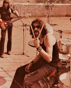 a man sitting on top of a drum kit next to another person holding a guitar