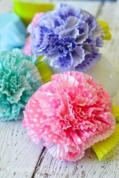 three colorful paper flowers sitting on top of a white wooden table next to each other