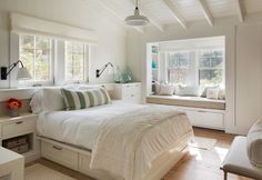 a bedroom with white walls and wooden flooring is pictured in this image, there are two windows on each side of the bed