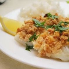 a white plate topped with fish and rice next to a lemon wedge on a table