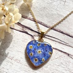 This delicate heart necklace features vibrant blue forget me nots framed in a gold toned stainless steel heart pendant.  The heart pendant hangs on an 18 inches long stainless steel chain (longer chains may be arranged if required). Blue Dainty Necklace With Heart Charm, Blue Flower Charm Jewelry As Gift For Her, Dainty Blue Necklace With Heart Charm, Blue Dainty Jewelry For Valentine's Day, Dainty Blue Heart-shaped Necklace, Blue Heart Pendant Jewelry Gift For Her, Blue Heart-shaped Jewelry For Mother's Day, Blue Heart Pendant Jewelry For Mother's Day, Heart-shaped Charm Necklace With Flower For Gift