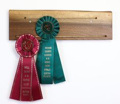 two ribbons are hanging from a wooden plaque holder on a white wall, one is green and the other is red