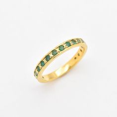 a yellow gold ring with green stones on the inside and outside, set against a white background