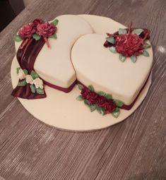 two heart shaped cakes on a plate with red and white flowers around the edges, sitting on a wooden table