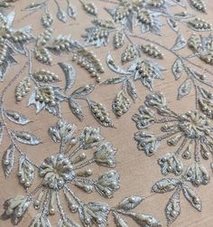 an embroidered fabric with silver flowers and leaves on beige background, close - up photo