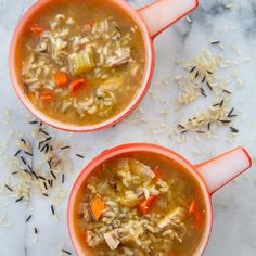 two orange bowls filled with soup on top of a white tablecloth next to rice and carrots