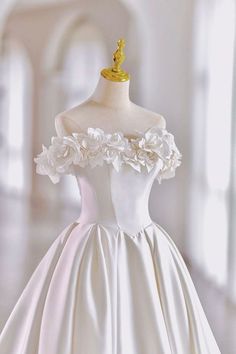 a white wedding dress with flowers on the shoulders and shoulder, in front of a mannequin