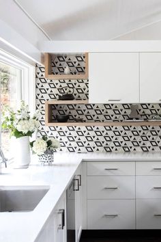 a white kitchen with black and white tile backsplash, wooden shelves, and flowers in vases