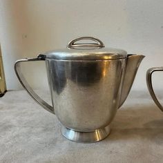 two silver teapots sitting next to each other on a white carpeted floor