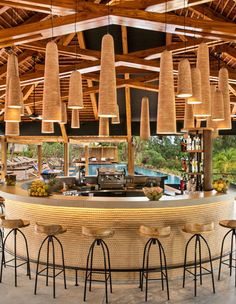 an outdoor bar with lots of stools and lights hanging from the ceiling above it