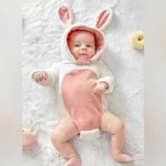 a baby wearing a bunny costume laying on top of a white blanket