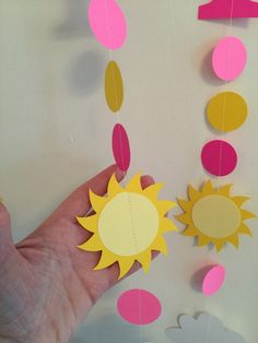 a hand is holding up some paper sun and moon decorations hanging from the side of a wall