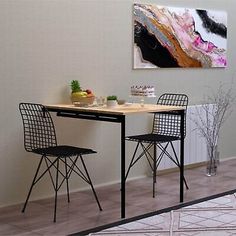 a dining table and two chairs in front of a wall with a painting on it