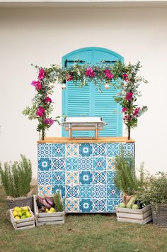 a blue and white tiled cabinet with flowers on the top, fruit in baskets below