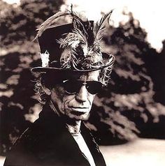 a man wearing a hat and sunglasses with feathers on it's head is looking at the camera