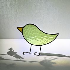 a glass bird sitting on top of a table next to a shadow cast by a person