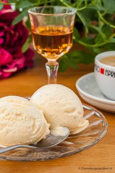 two scoops of ice cream sit on a glass plate next to a cup of tea