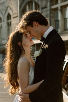 a man and woman standing next to each other in front of a car with their arms around each other