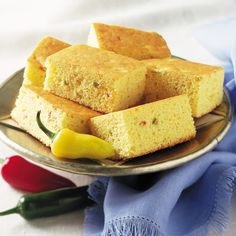 several pieces of cornbread on a plate next to peppers and a blue cloth,