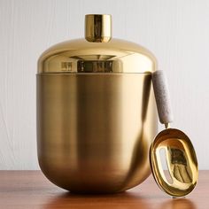 a gold colored ice bucket and spoon on a wooden table