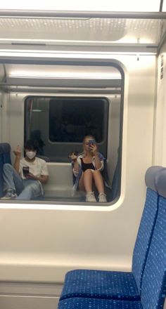 two people sitting on a train looking at their cell phones while wearing protective face masks